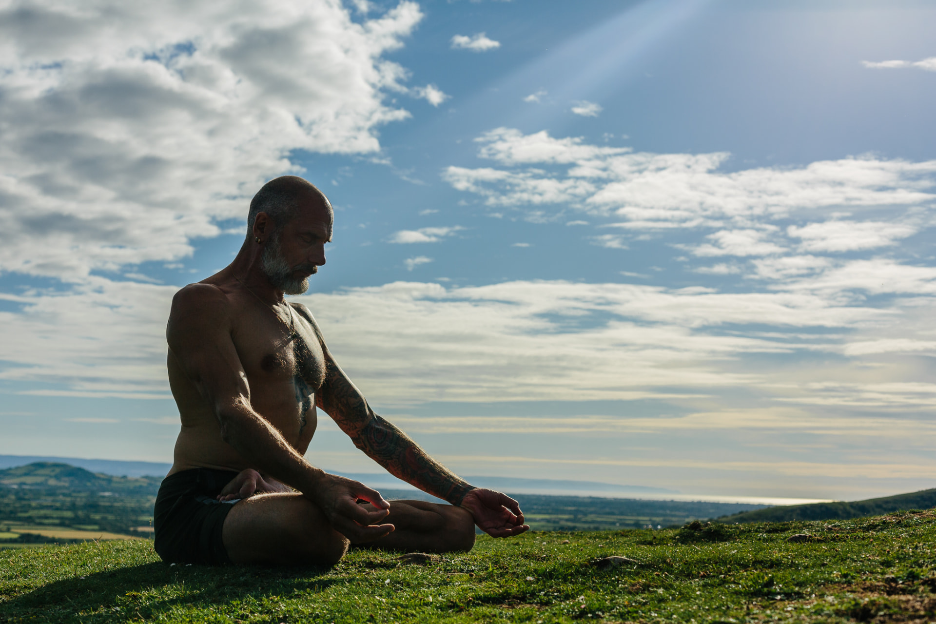 Christopher Gladwell in seated meditation on a hilltop beneath a dramatic sky