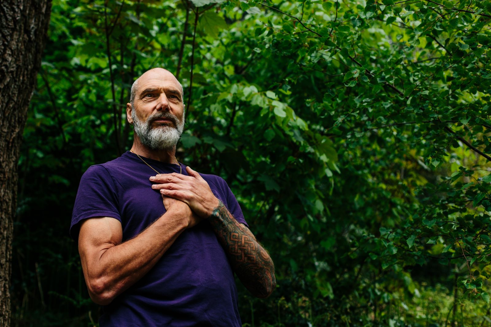 Christopher Gladwell standing in woodland with his hand resting on his chest, looking upward