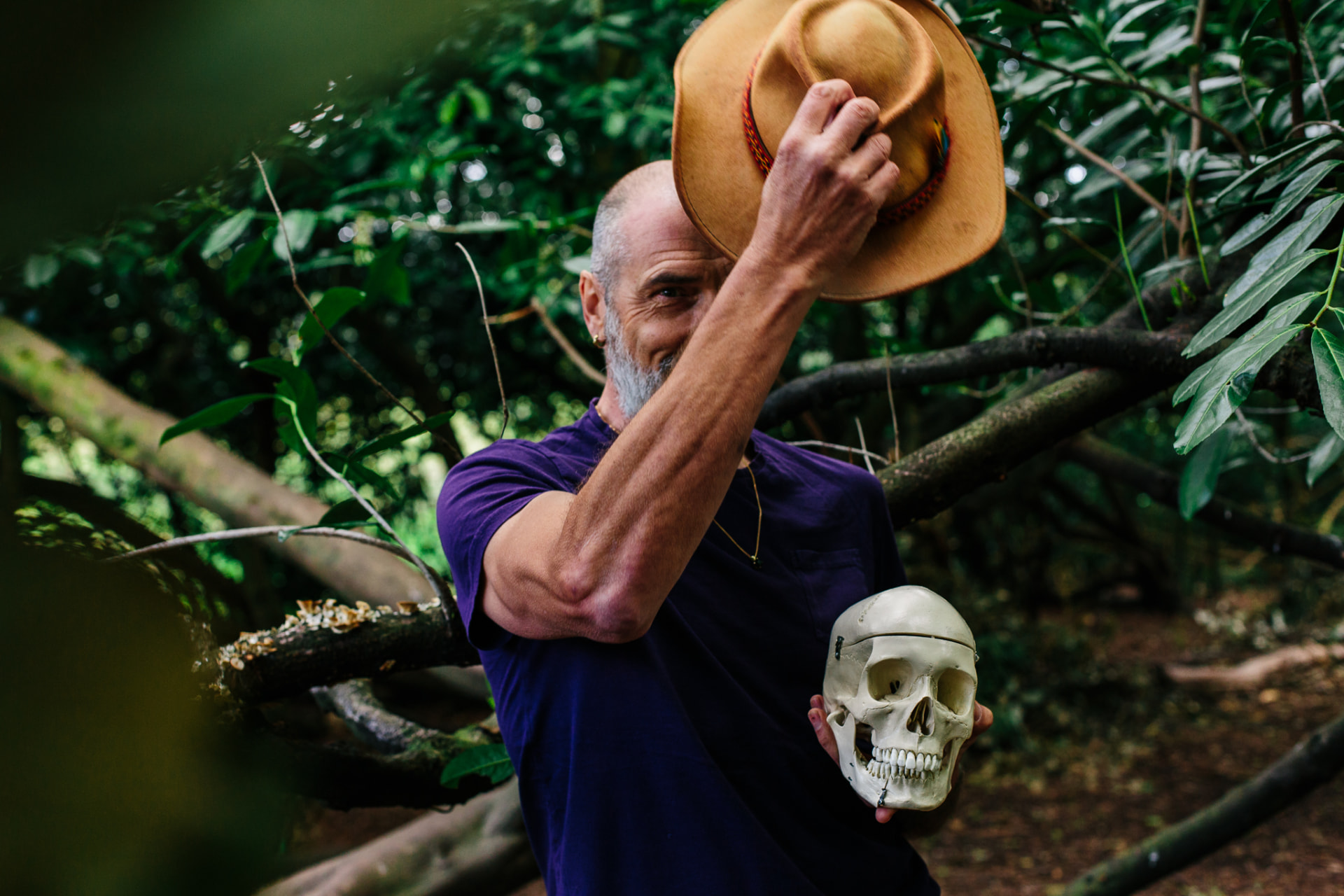 Christopher Gladwell in woodland, raising a wide-brimmed hat and holding a skull